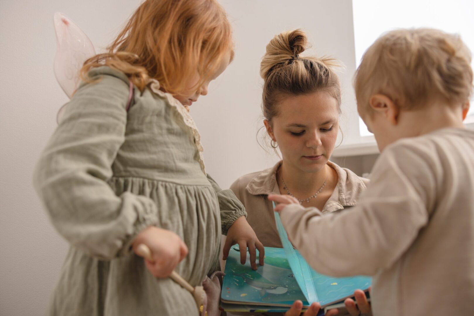 young parent mother plays with children shows pictures book her daughter son home real lifestyle people concept